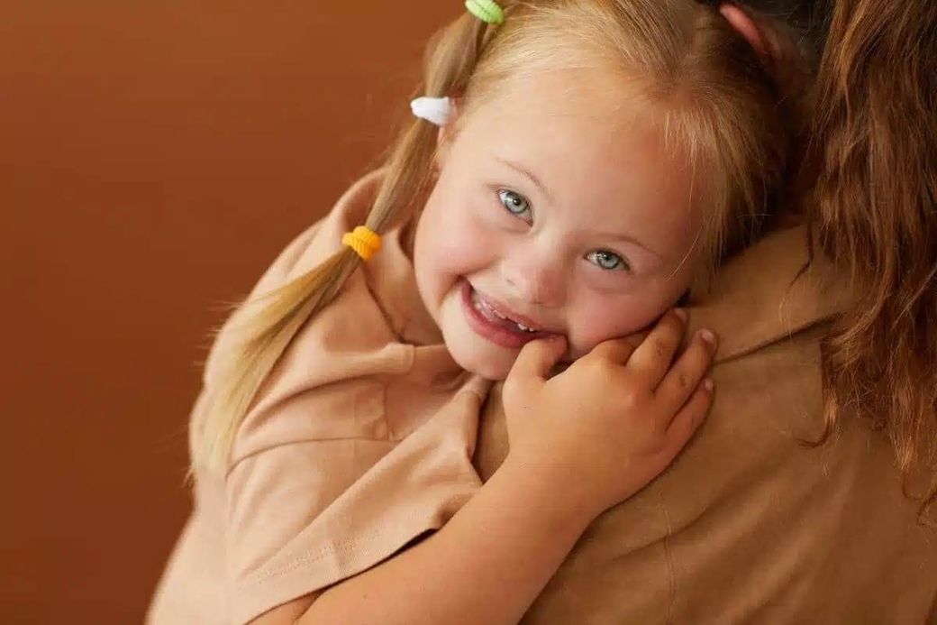 Laughing girl with Down syndrome hugging an adult